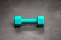 Dumbbell in a silicone shell of turquoise color on the gray floor