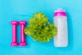 Dumbbells, bottle of water and salad leaves on yoga mat