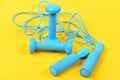 Dumbbells and jump rope in cyan blue color on yellow Royalty Free Stock Photo