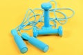 Dumbbells and jump rope in cyan blue color on yellow Royalty Free Stock Photo