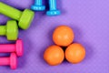 Dumbbells and orange fruits on purple texture background. Royalty Free Stock Photo