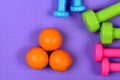 Dumbbells and orange fruits on purple texture background. Royalty Free Stock Photo