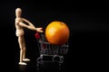 Dummy pushing a shopping cart with an orange on black background. Symbol of commerce