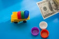 Dump truck with colored plastic bottle caps on blue background. 100 Dollars on table. Make money on Recycling Plastic, Bottles,