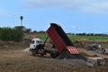 Dump truck dumping black sand on a fresh work site