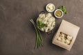 Dumplings in eco-friendly paper packaging for delivery and a bowl with dumplings, onions and sauces on a dark background