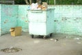 A dumpster with overflowing garbage and an empty box in a fenced waste storage area.Garbage collection in the city