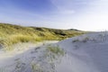 Dunes in the morning sunlight. Gras grow on the hilltops. In the blue sky, white clouds move to the sea. Royalty Free Stock Photo