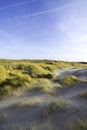 Dunes in the morning sunlight. Grasses grow on the hilltops. In the blue sky, white clouds move to the sea. Beach in the Royalty Free Stock Photo