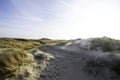 Dunes in the morning sunlight. Grasses grow on the hilltops. In the blue sky, white clouds move to the sea. Beach in the Royalty Free Stock Photo