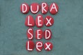 Dura lex, sed lex, a maxim of Roman civil law composed with red colored stone letters on green sand