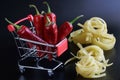 Durum fettuccine pasta and red hot chili peppers in a supermarket trolley against a dark blue background. The concept of buying