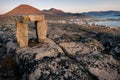 Dusk in a harsh arctic landscape with bare hills and ocean. Inuksuk with Inuit settlement of Qikiqtarjuaq in the