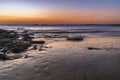 Dusk over the ocean with orange and purple sky reflecting on the beach Royalty Free Stock Photo