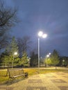 Dusk in the Park A Bench Under the Lamplight with Trees and a Cloudy Sky Royalty Free Stock Photo