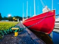 Dusk view on red bow of old sailboat moored with rope to metal bollard or hook on a coast Royalty Free Stock Photo