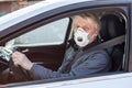 Dust facial mask is on elder man face while driving a car, Caucasian driver inside a vehicle