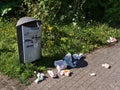 Dustbin in park area in Koblenz with package waste lying around with grass and bushes. Royalty Free Stock Photo