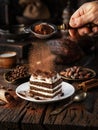 Dusting tiramisu-like cake with cocoa powder. Still life with slice of cake and coffee and cacao beans on wooden table