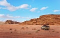 Dusty desert with rocky massif and blue sky above, off road desert vehicle in foreground. Typical scenery in Wadi Rum Royalty Free Stock Photo