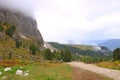 Dusty road leading to the peaks of the Dolomites covered with fog, gloomy sky background