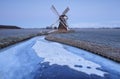 Dutch windmill in dusk by frozen river in winter