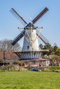 Dutch windmill with its blades with red lines with trees in the background, farmland with green grass, sunny day with clear blue Royalty Free Stock Photo