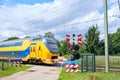 Dutch yellow high speed intercity train passing a closed railway crossing with closed barriers and blinking red lights