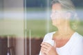 Dwelling on the past. A thoughtful senior woman looking out of her window while enjoying some coffee. Royalty Free Stock Photo