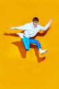Dynamic fashion moment as young man leaps in modern, comfy attire against striking yellow background. Style meets action