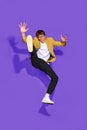 Dynamic fashion moment as young man leaps in modern, office suit and glasses against vibrant purple background. Style