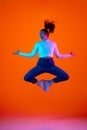 Dynamic fashion. Young woman dressed trendy outfit posing in mid-air against gradient orange-pink background in neon