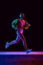 Dynamic image of sportive young girl in sportswear, jacket and headphones training, running on black background in neon
