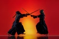 Dynamic image of two men, professional kendo athletes training with bamboo shinai sword against gradient red studio Royalty Free Stock Photo