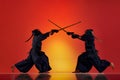 Dynamic image of two men, professional kendo athletes training with bamboo shinai sword against gradient red studio Royalty Free Stock Photo