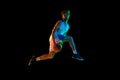 Dynamic image of young man, basketball player in mid-air, training, jumping with ball against black background in neon