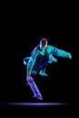 Dynamic image of young man in casual clothes in motion, training, skateboarding against black studio background in neon