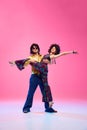 Dynamic portrait of dancers duo, man and woman, posing in retro fashion clothes against gradient pink studio background.