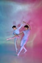 Dynamic portrait of two ballet dancers in white leotards dancing contemporary moves under colored lighting against Royalty Free Stock Photo