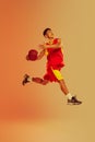 Dynamic portrait of young man, basketball player throwing ball into basket  over orange studio background in Royalty Free Stock Photo