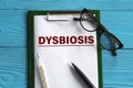 DYSBIOSIS - word in a notepad on a blue background with a pen, glasses and a thermometer