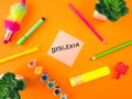 Dyslexia word on sticky note with child supplies on orange background. Learning difficulty, education concept