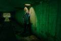 Dystopian portrait of model posing in the river of sewage in tunnel under city. Lit with green light