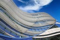 Ow angle view on curved steel, glass, natural building facade with wavy lines against clear blue sky