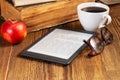 E-book, cup of coffee, apple and glasses next to a stack of vintage books in the library. Education concept