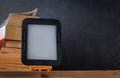 E-book reader on the wooden stand next to the stack of paper books at the black background Royalty Free Stock Photo