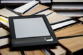 The e-book with a white screen lies on the open multi-colored books that lie on a dark background, close-up