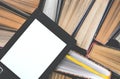 The e-book with a white screen lies on the open multi-colored books that lie on a dark background, close-up Royalty Free Stock Photo