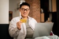 E-commerce concept. Happy asian mature man holding credit card and shopping online with laptop, sitting on couch at home Royalty Free Stock Photo