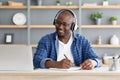 E-education. Happy black mature man using laptop and taking notes, listening online course Royalty Free Stock Photo
